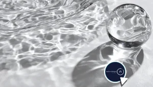 Close-up of water and crystal casting sharp caustic light patterns on a white surface with a chrome sphere, illustrating V-Ray 7 GPU caustics.